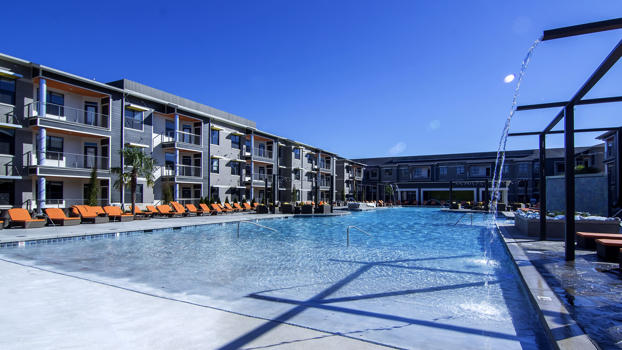 Sparkling outdoor swimming pool surrounded by modern apartment buildings under a clear blue sky at a luxury West Little Rock